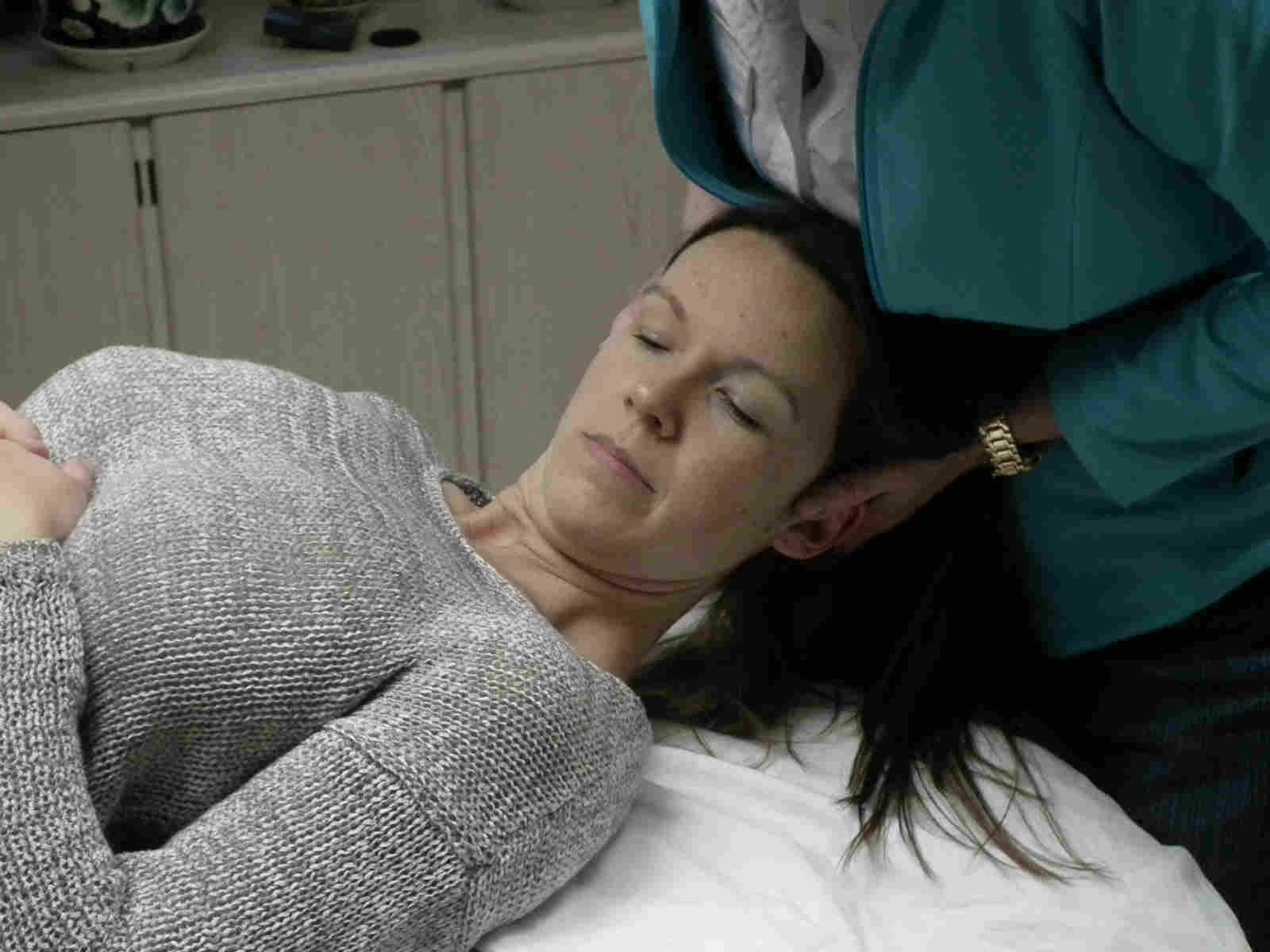 A woman laying on top of a bed with another person touching her head.